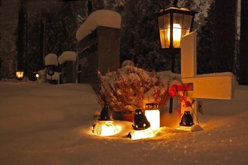 Kynttilät lumen keskellä hautaristin edessä.